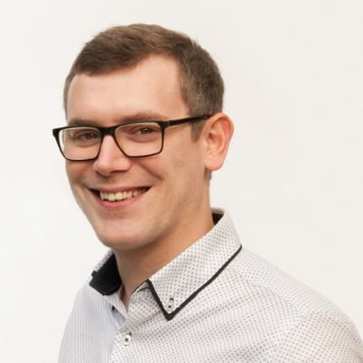 A smiling man with glasses, wearing a white polka-dot shirt against a plain white background.