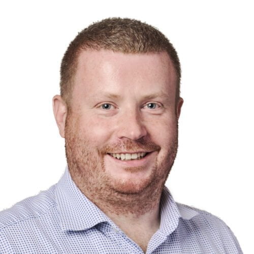 Headshot of a smiling man with short red hair, wearing a blue polka-dot shirt against a white background.