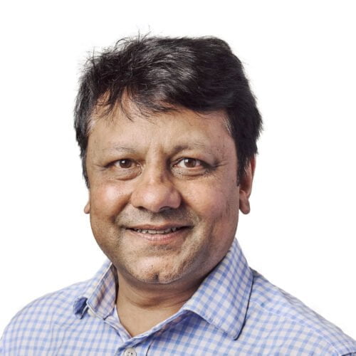 Portrait of a smiling middle-aged man with black hair, wearing a blue checkered shirt against a plain white background.