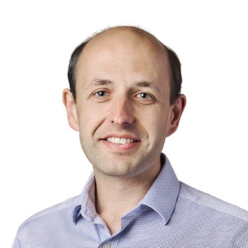 Portrait of a smiling bald man wearing a blue checkered shirt against a white background.
