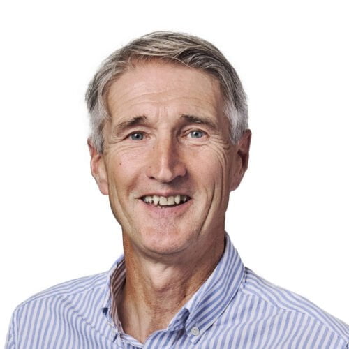 Portrait of a smiling older man with gray hair, wearing a blue striped shirt against a plain white background.