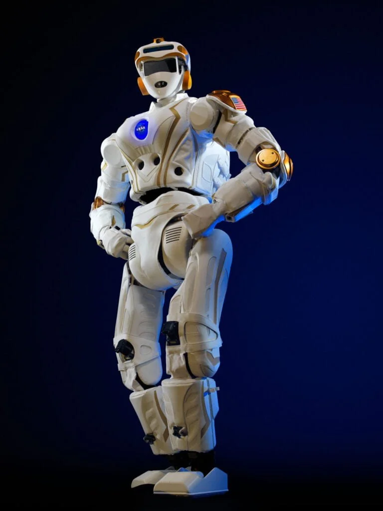 A futuristic white and orange humanoid robot standing against a dark blue background.