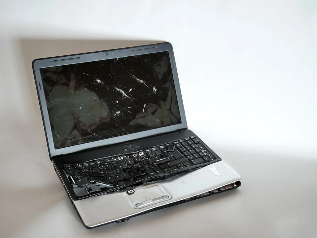 A damaged laptop with a cracked screen and missing keys, displayed on a plain white background.