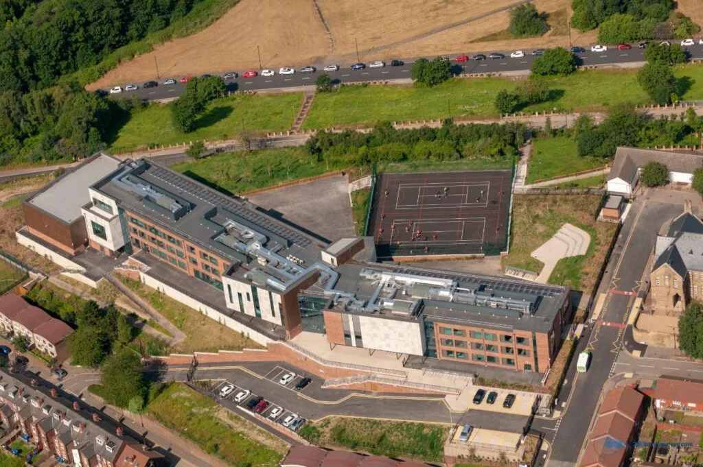 Aerial view of a modern school complex with tennis courts and adjacent parking, surrounded by grade 2 listed residential streets.