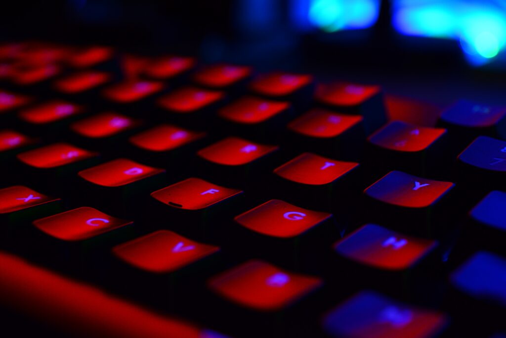 Close-up of a backlit keyboard with red illumination on the keys, highlighting letters in a dark environment.