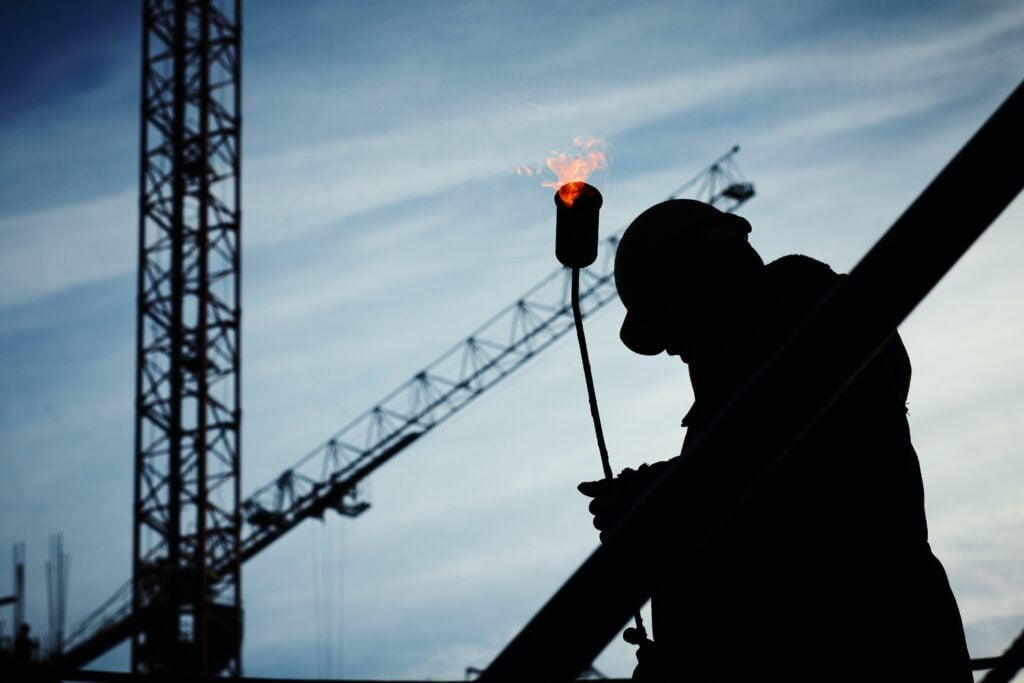 Silhouette of an IT services worker holding a glowing torch with cranes in the background against a dusk sky.