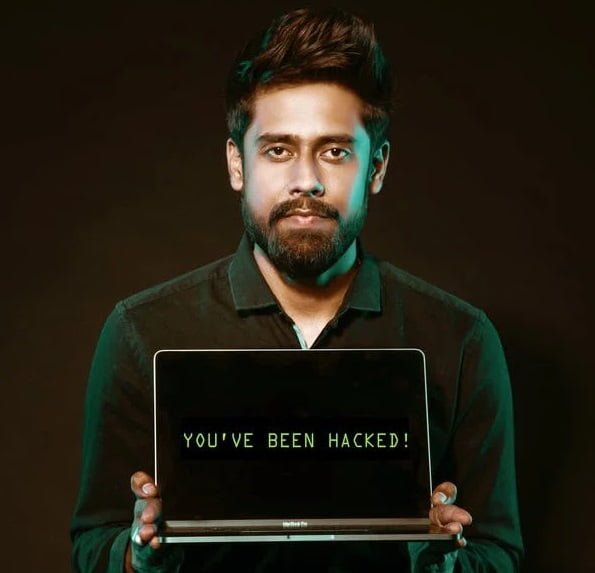 A man with a beard holds a laptop displaying the message "you've been hacked!" on a dark background, symbolizing threats in cyber security for businesses.