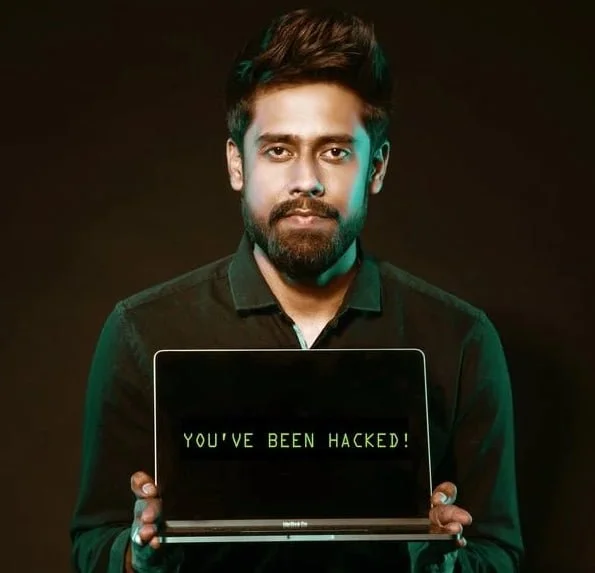 A man with a beard holds a laptop displaying the message "you've been hacked!" on a dark background, symbolizing threats in cyber security for businesses.