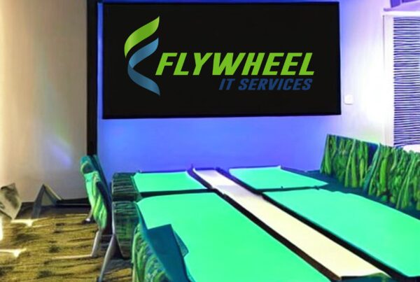 A modern conference room with green and blue lighting, featuring AV solutions for business and a large screen displaying the logo of "flywheel it services.