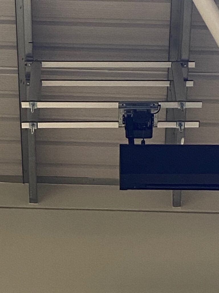 A security camera mounted on the underside of a wooden staircase with an attached video wall.