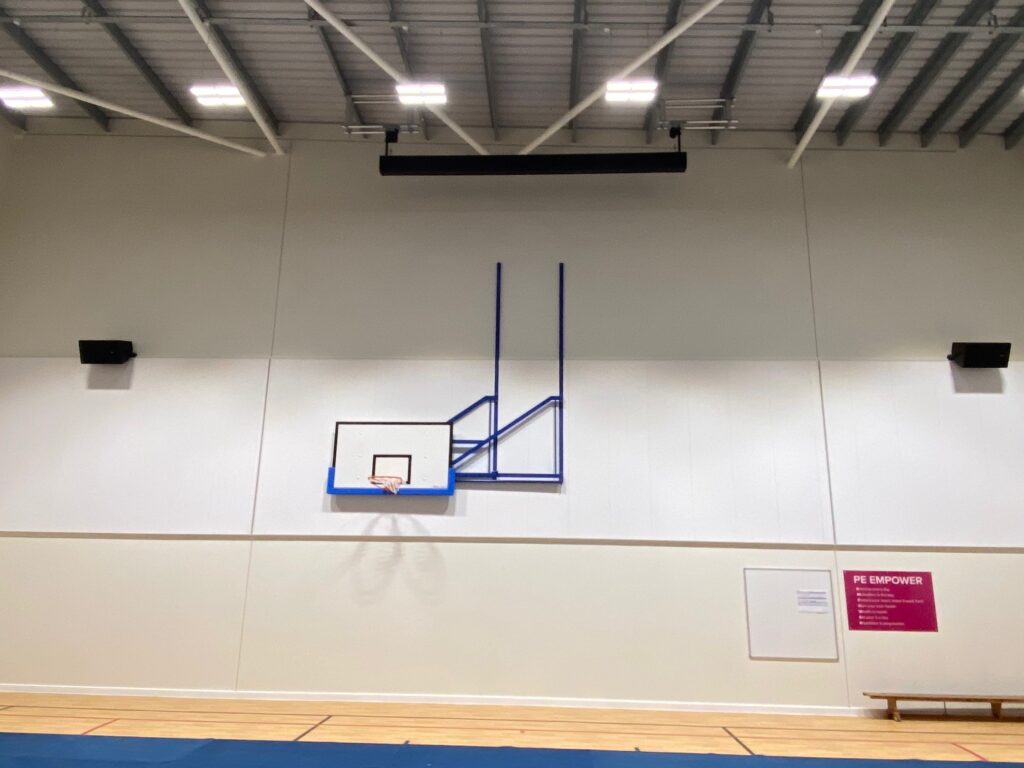 Indoor basketball court with one hoop mounted on a video wall, under bright lights, with a blue banner reading "empower" in the background.