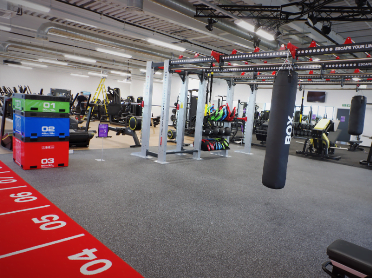 A modern, well-equipped leisure centre with various exercise stations, including weight lifting areas, boxing bags, and treadmills, featuring a prominent red and black color scheme.