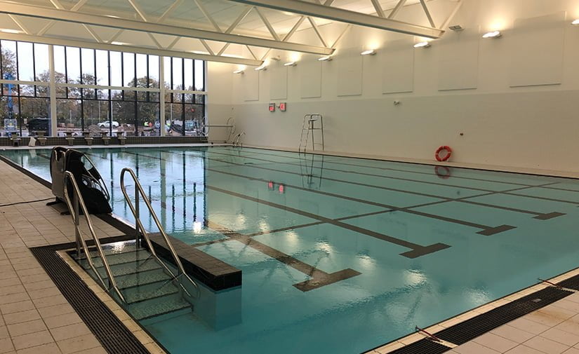 Indoor swimming pool at the leisure centre with clear water, marked lanes, starting blocks on the left, and large windows letting in natural light.