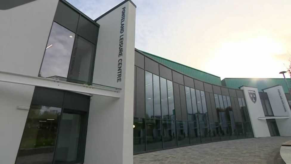 Exterior view of the leisure centre with a prominent sign, featuring large glass windows and a modern architectural design.