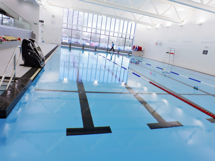 Indoor swimming pool at the leisure centre with clear blue water, lane dividers, and large windows with a lifeguard on duty.