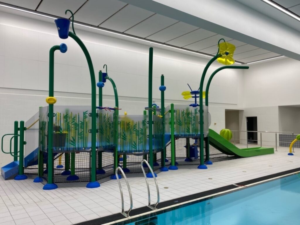 Leisure centre with an indoor swimming pool featuring a colorful water playground with slides, sprayers, and climbing structures.