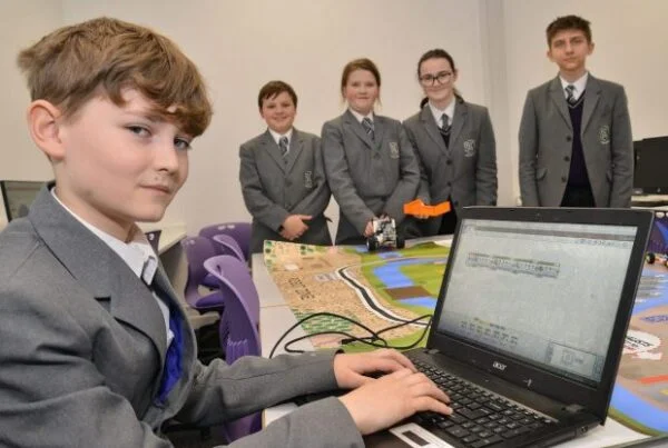 Five students in school uniforms using a computer and robotic equipment in a classroom with a school backup solution.