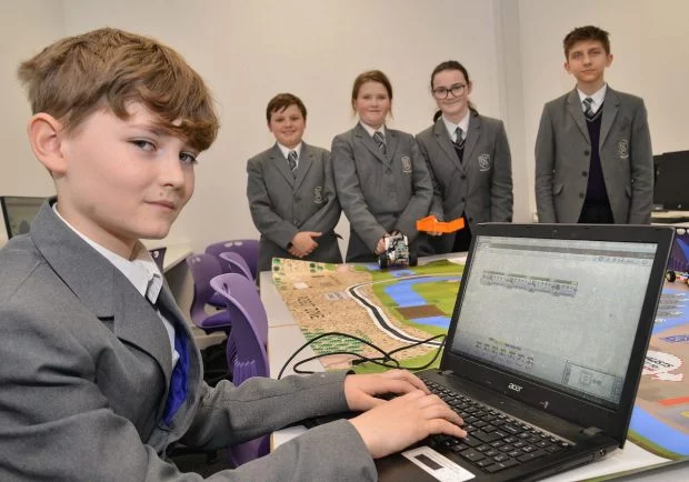 Five students in school uniforms using a computer and robotic equipment in a classroom with a school backup solution.