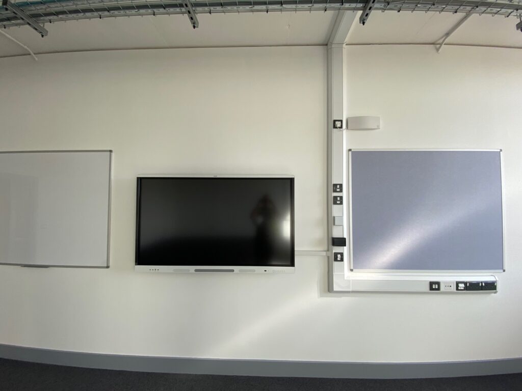 Modern office meeting room with advanced audio visual systems including a large TV screen flanked by two whiteboards on a curved white wall.