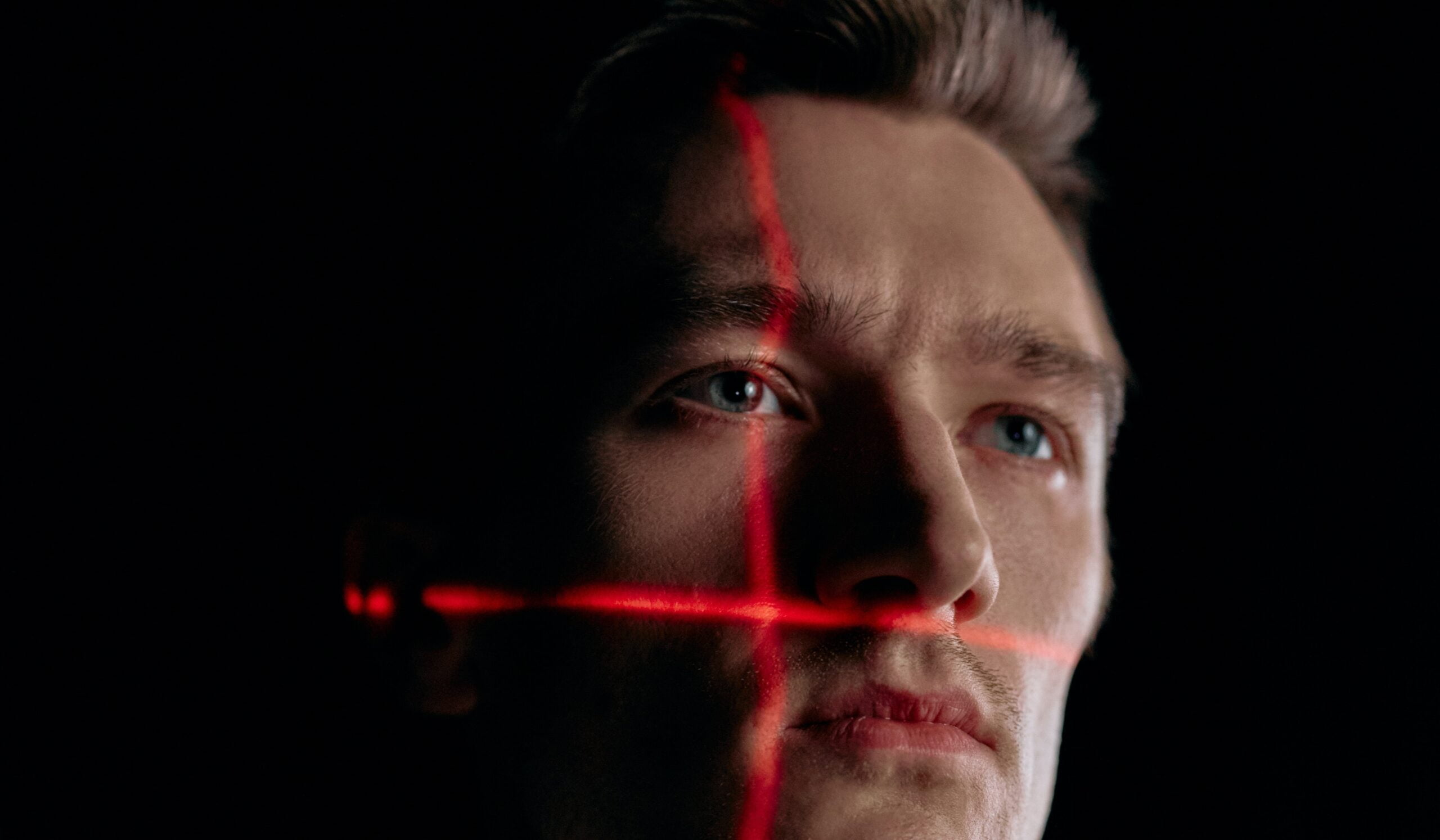 Close-up of a man's face illuminated by a red cross light beam from business access control systems in a dark ambiance.
