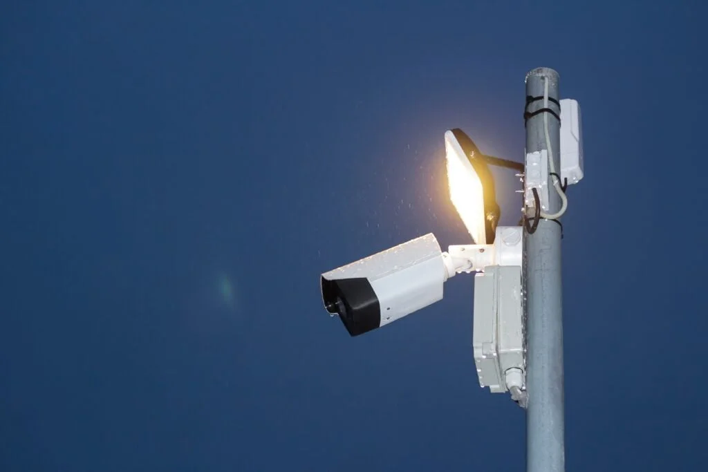 Outdoor security camera and various types of CCTV cameras attached to a pole against a clear blue sky.