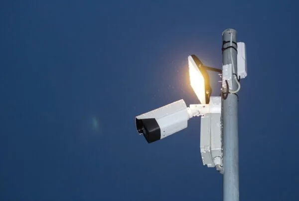 Outdoor security camera and various types of CCTV cameras attached to a pole against a clear blue sky.