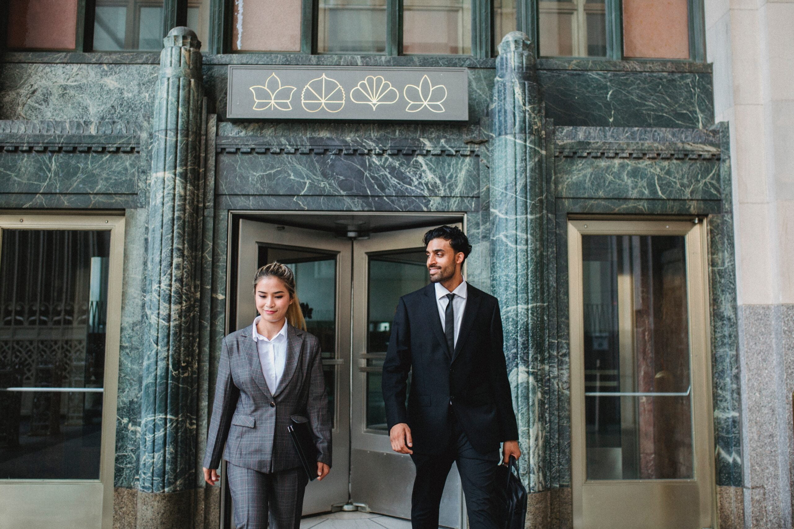 Two business professionals exiting a building with a green marble facade and decorative doorway equipped with business access control systems.