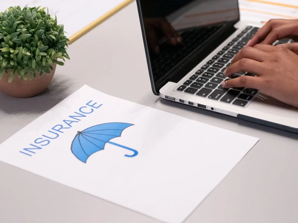 A person working on a laptop next to a printed paper labeled "cyber liability insurance" with a blue umbrella icon, indicating a focus on insurance topics.