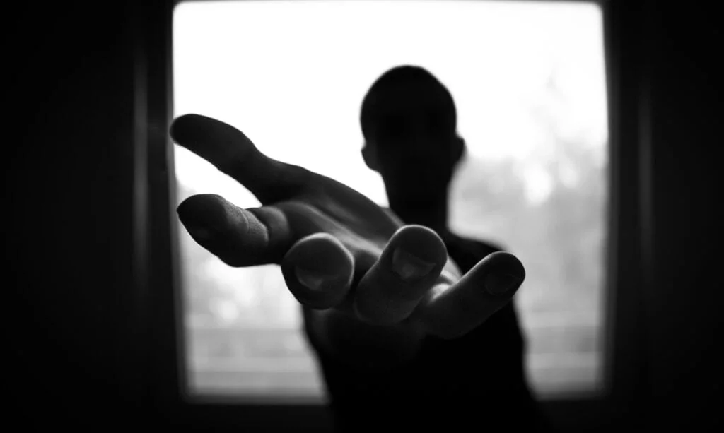 Silhouette of a person spoofing a handshake towards the camera, with a blurred background visible through a window.