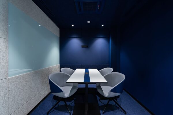 Small modern meeting room with AV solutions for business, a white table, four chairs, blue walls, and subtle lighting.