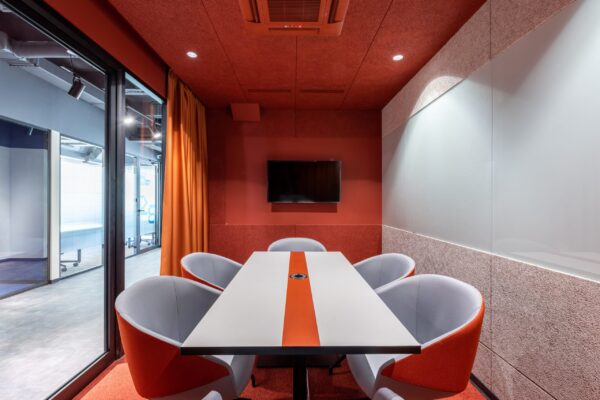 Modern office meeting room with a white table, orange chairs, and a red carpet, featuring AV solutions for business and glass walls.