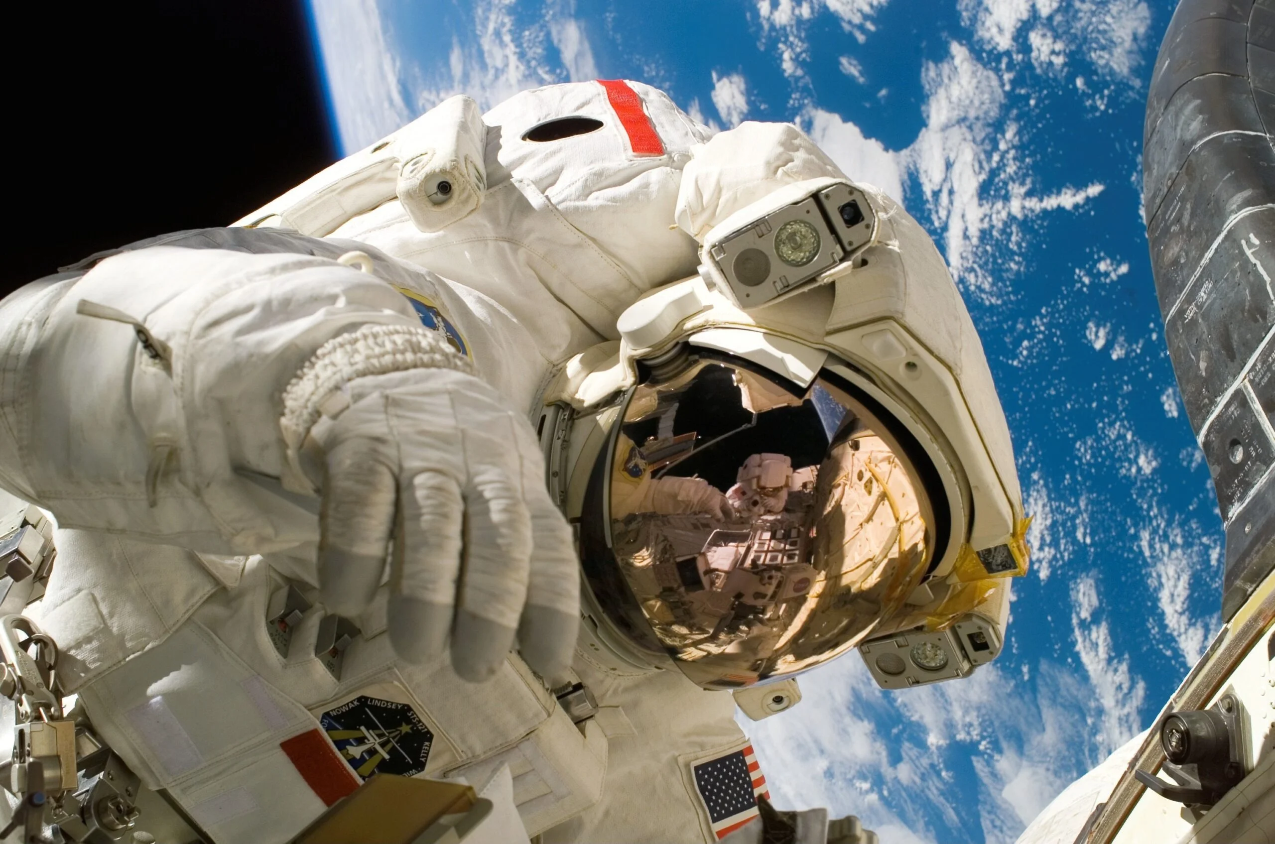 Astronaut in a white spacesuit with a reflective visor floating in space, with earth visible in the background.
