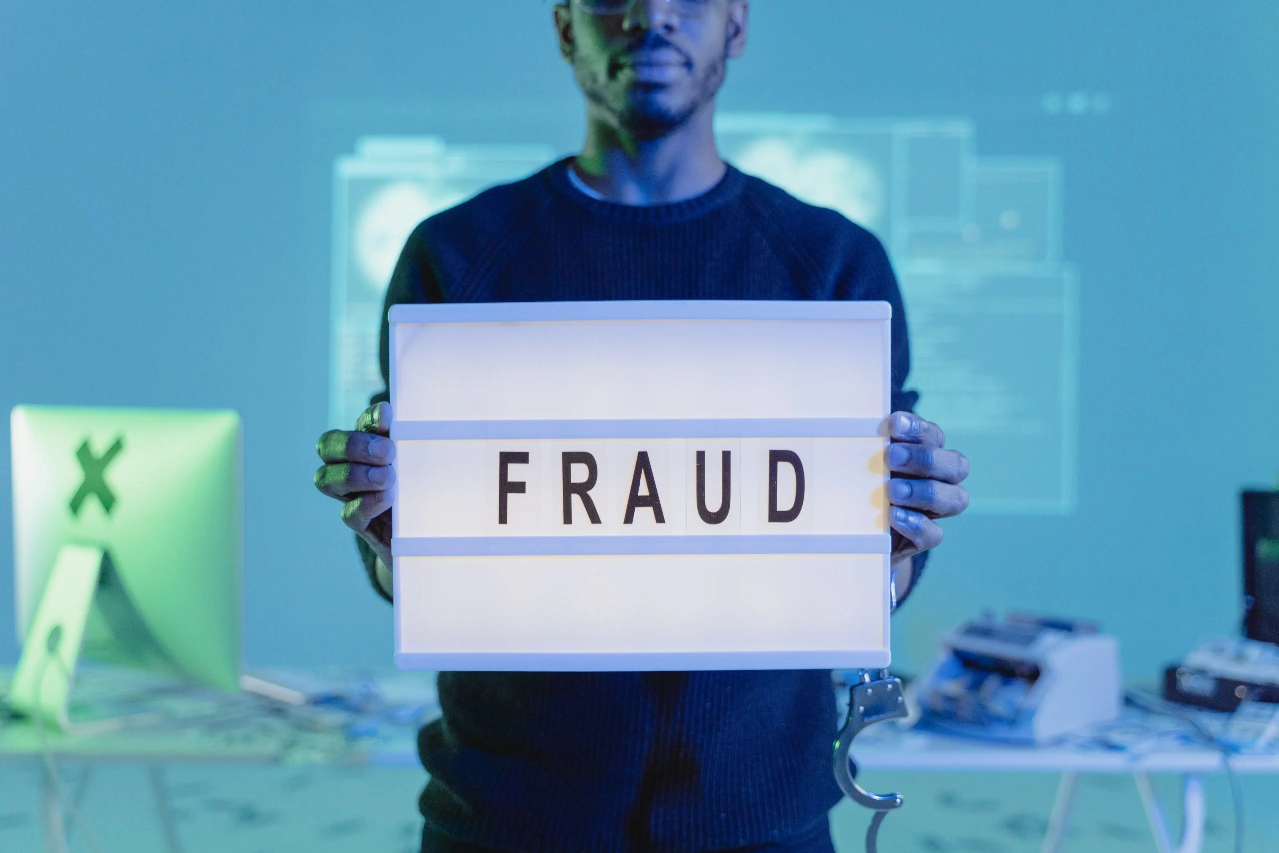 Man holding a lightbox displaying the word "fraud" in a tech environment with computers and digital projections in the background.