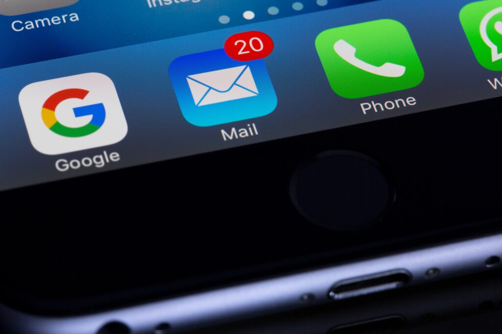 Close-up of a smartphone screen displaying app icons with a focus on the mail app icon showing 20 unread emails, emphasizing the need for effective spam filters.