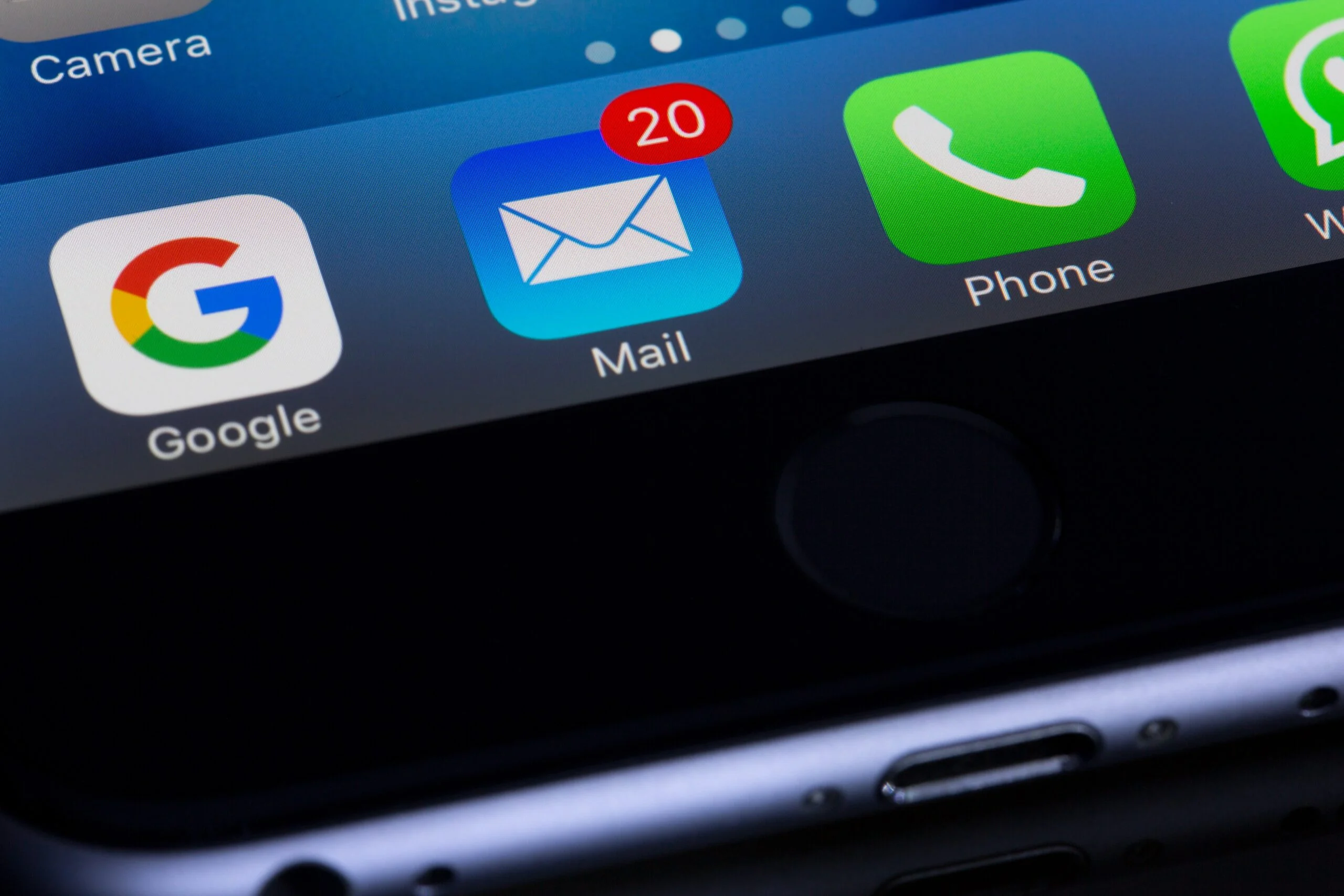 Close-up of a smartphone screen displaying app icons with a focus on the mail app icon showing 20 unread emails, emphasizing the need for effective spam filters.