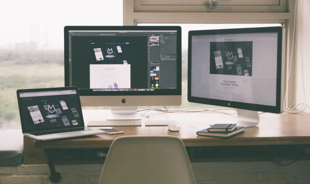 A workspace with three computers displaying IT procurement services on their screens, a chair in front, and a notebook on the table.