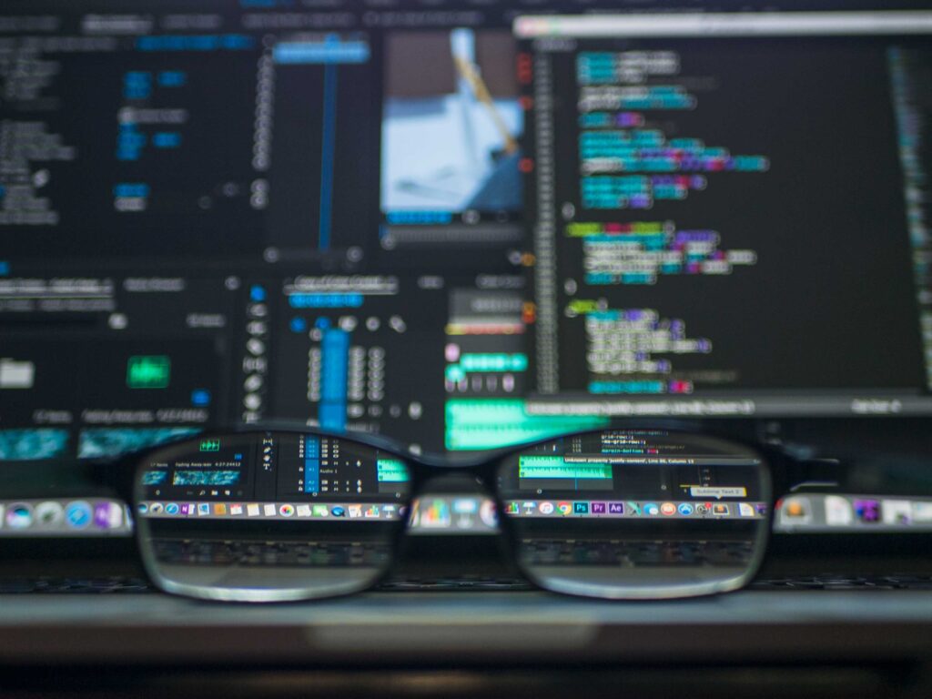 Eyeglasses in focus, resting before computer screens displaying colorful low code development platforms and data analysis.
