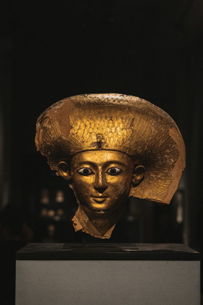An ancient egyptian sarcophagus mask with a gold and blue headdress, displayed in a museum.