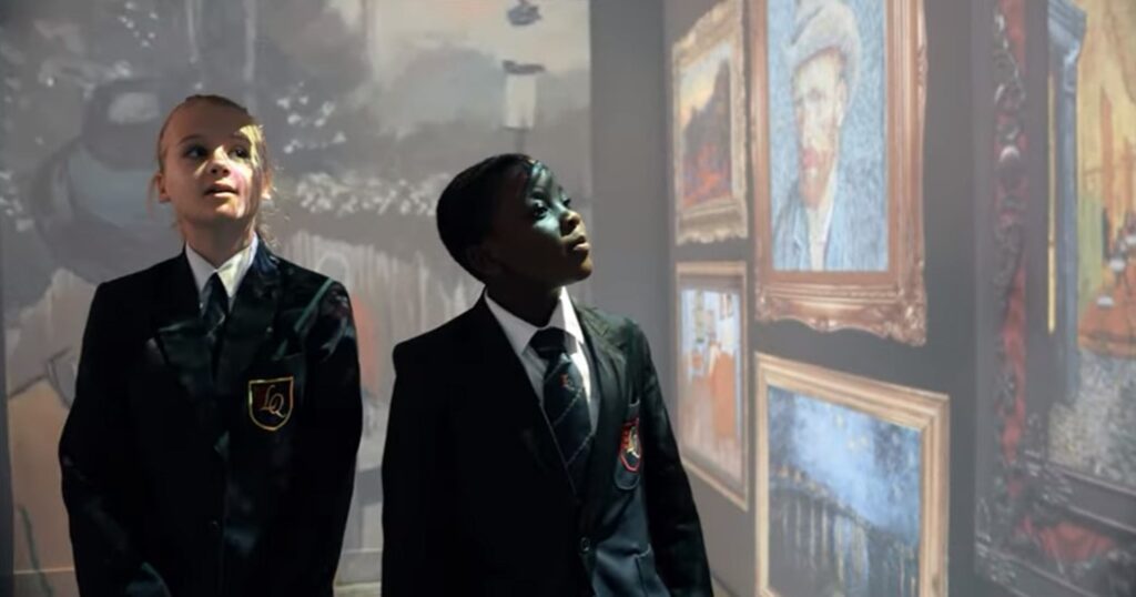 Two students in uniforms attentively looking at projected art images in a museum or gallery setting.