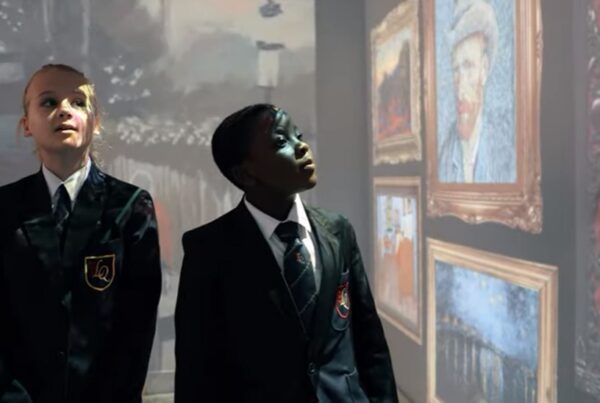 Two students in uniforms attentively looking at projected art images in a museum or gallery setting.