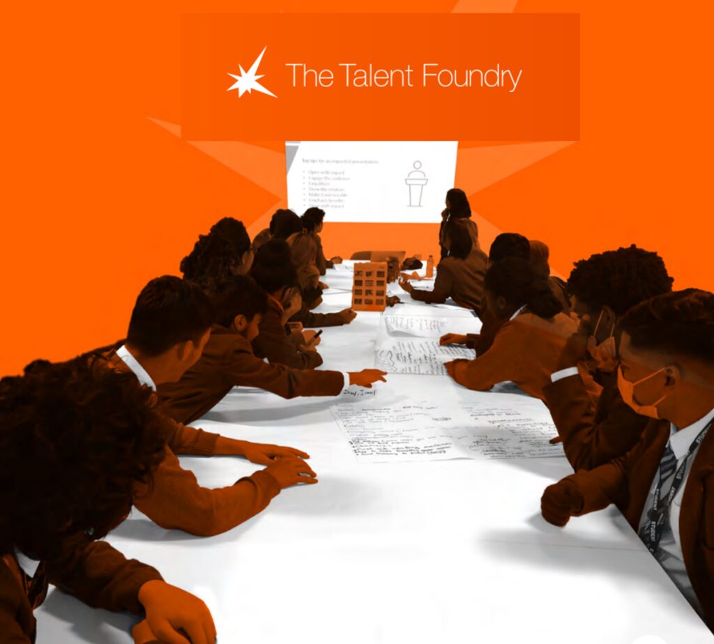 Group of students in business attire at a long table participating in a workshop, with "the talent foundry" logo displayed in the background.