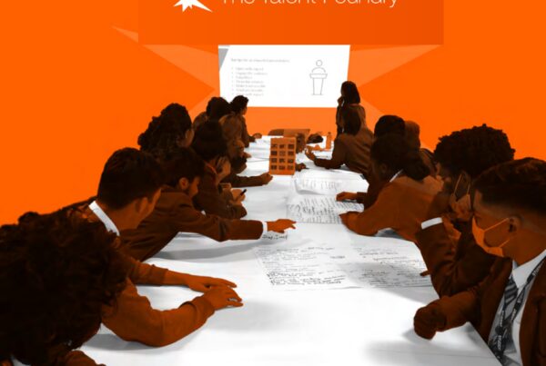 Group of students in business attire at a long table participating in a workshop, with "the talent foundry" logo displayed in the background.
