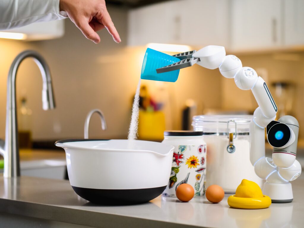 A robot arm in a kitchen pours sugar into a bowl, surrounded by ingredients and utensils on a countertop.