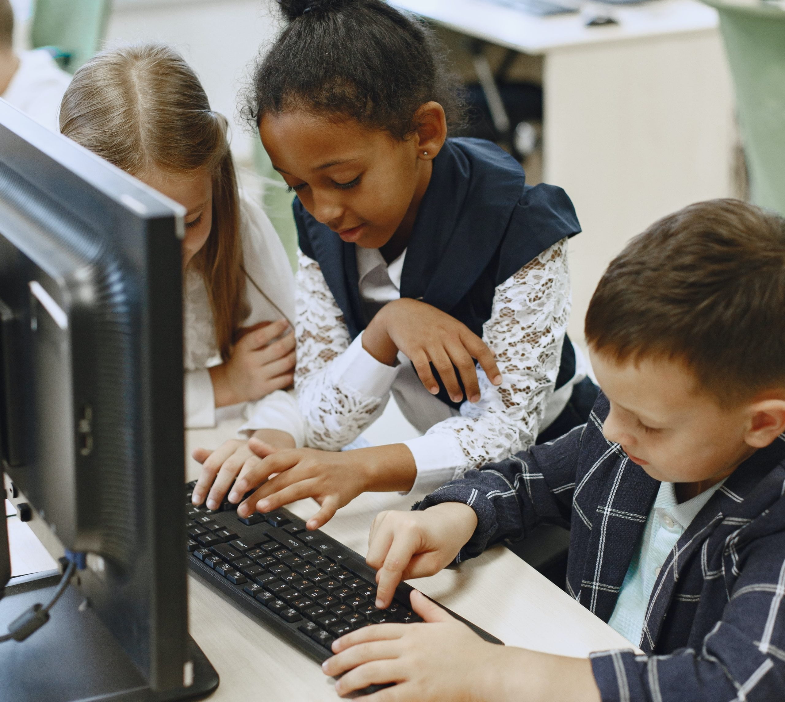 Three students, two girls and a boy, using a computer together in a classroom setting.