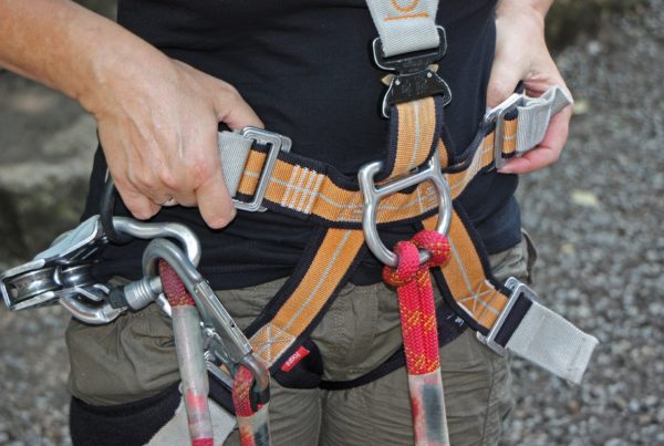 A person adjusting a climbing harness with carabiners and safety gear attached, ensuring everything is restored from a backup check.