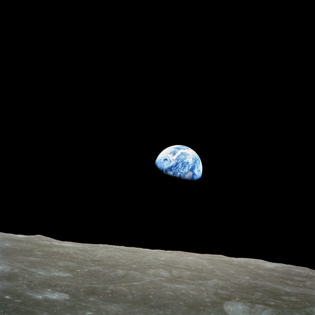 Earthrise viewed from the moon's surface, showing earth partially visible against the blackness of space, framed by the moon's horizon.