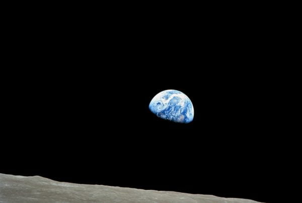 Earthrise viewed from the moon's surface, showing earth partially visible against the blackness of space, framed by the moon's horizon.