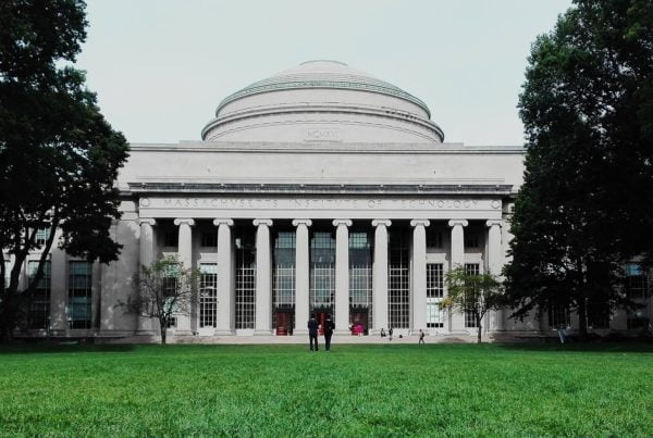Frontal view of the massachusetts institute of technology's great dome and entrance, flanked by trees, with people walking in front.