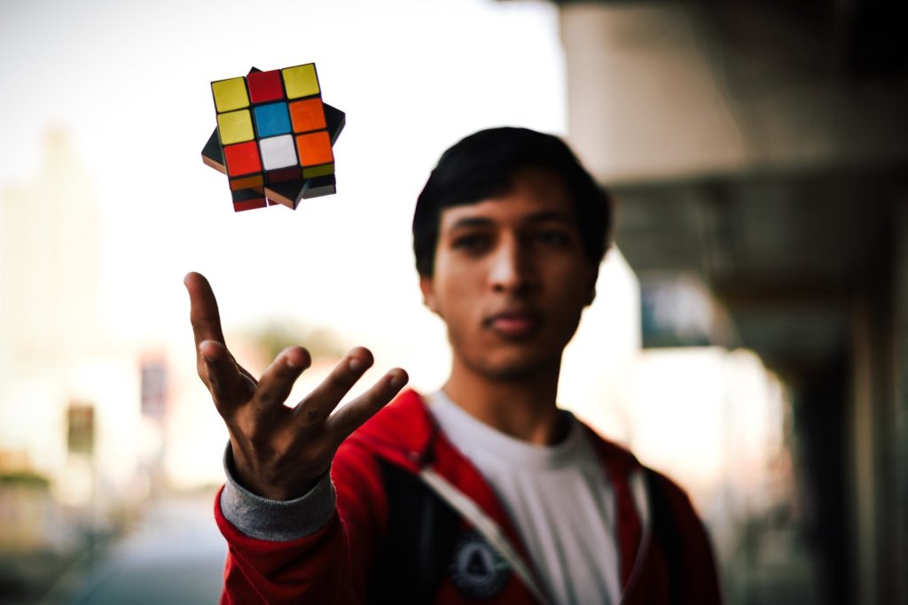 A young man tossing a Rubik's cube, captured in mid-air with a blurred background, illustrating the concept of solving complex compliance software issues.