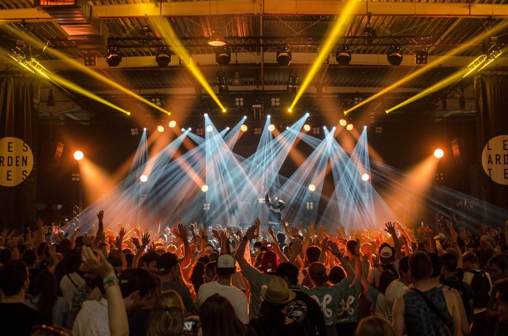 Crowd of people enjoying a concert with hands up, vibrant stage lights illuminating the venue from above, all compliant with Martyn's Law security measures.